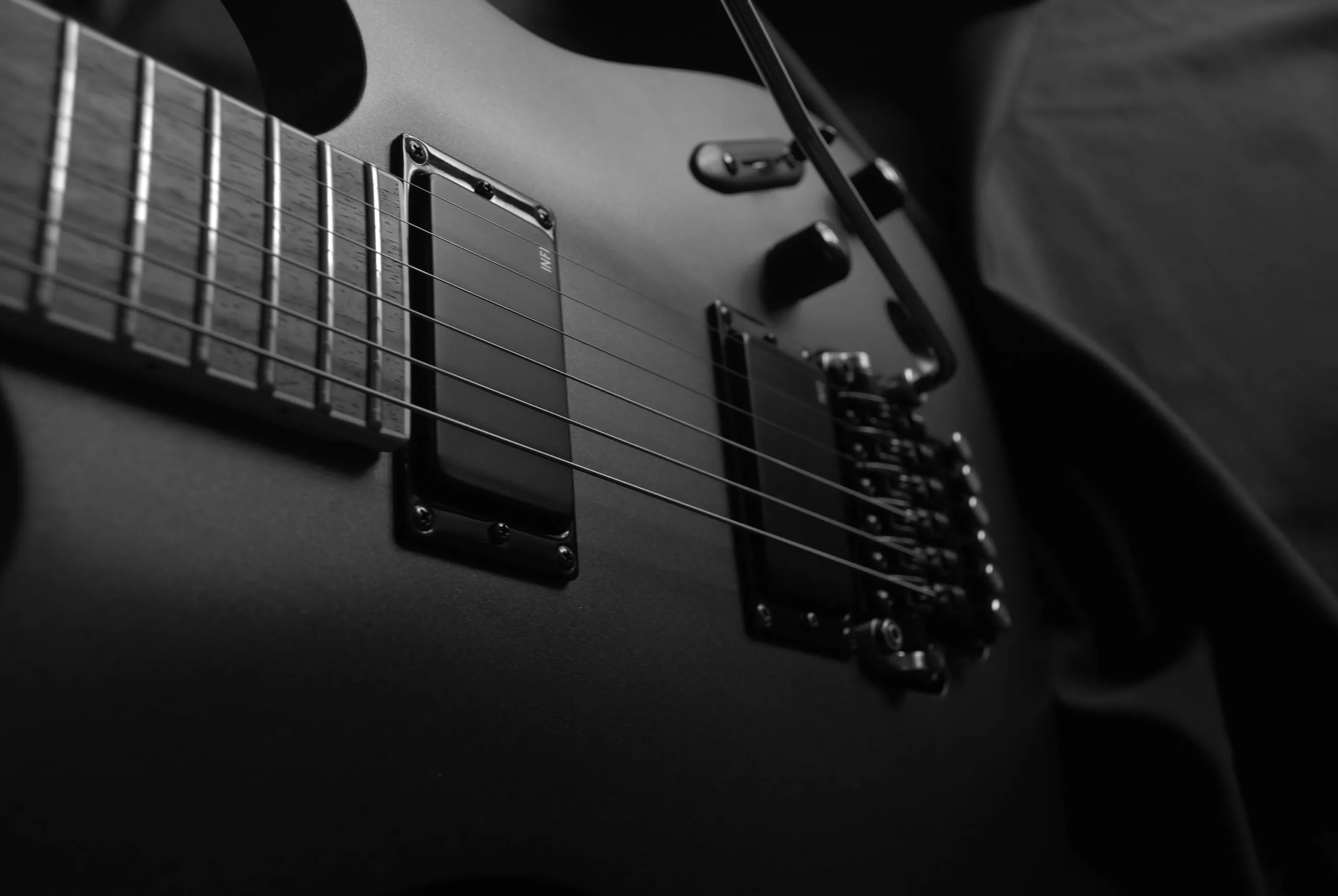Primer plano en blanco y negro del cuerpo de una guitarra eléctrica, con las cuerdas, los micrófonos y el puente en penumbra.