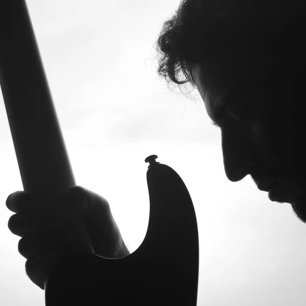 Franco Alcaraz a contraluz, de perfil y con la cabeza baja, sosteniendo una guitarra eléctrica, en blanco y negro.