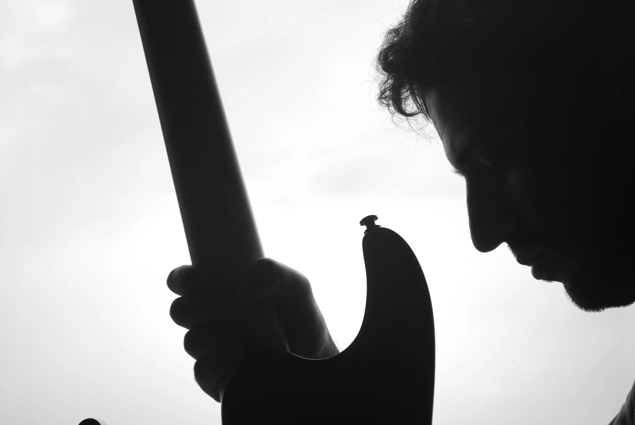 Silueta en blanco y negro de un músico de perfil, con la cabeza baja, que sostiene una guitarra eléctrica contra un cielo blanco.